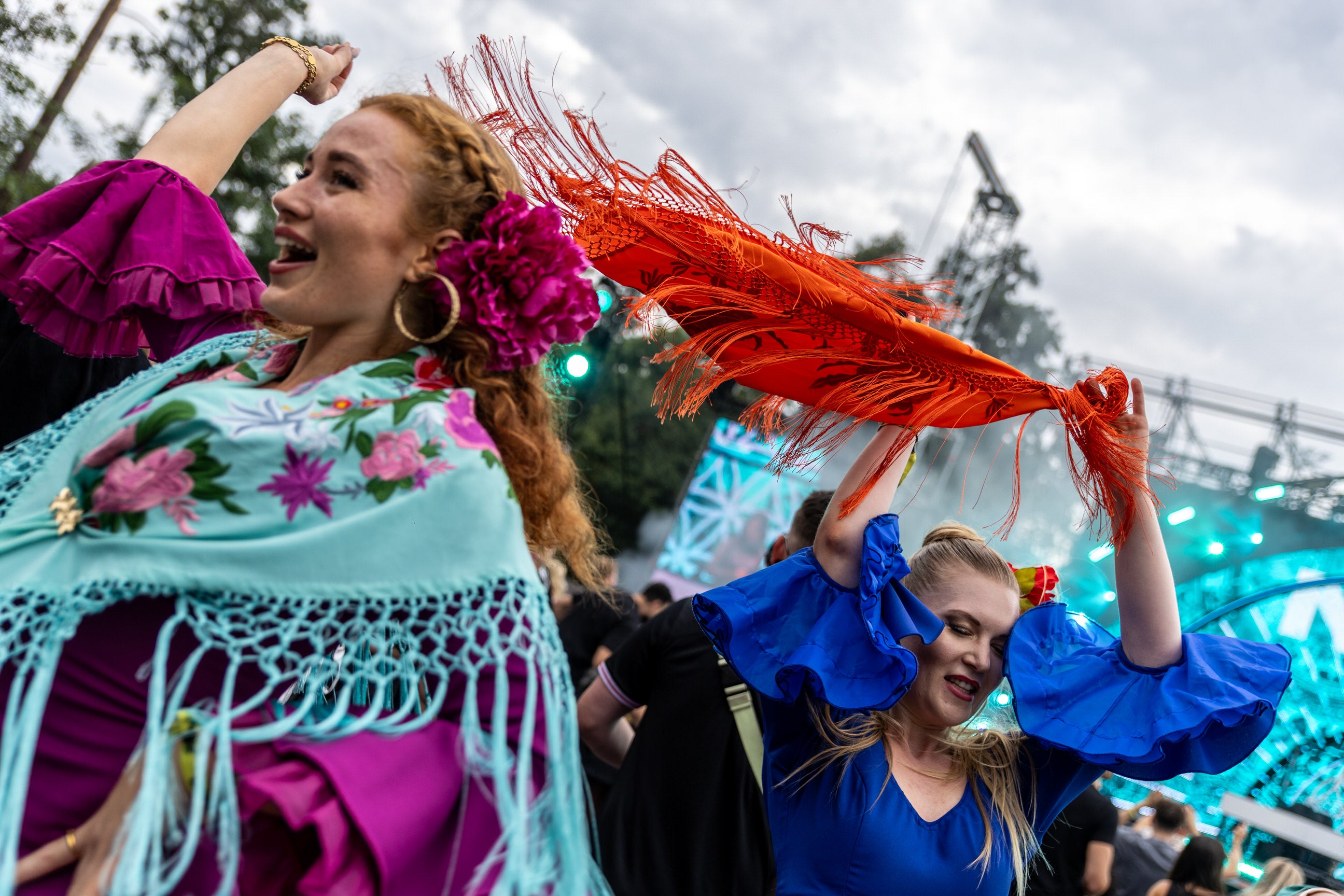 Two women in colorful traditional outfits dancing at an electronic music festival.